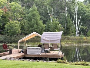 A wooden dock with a covered seating area, a grill, and a red chair.