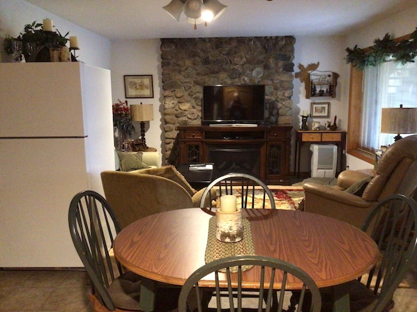 Una sala de estar acogedora con pared de piedra, televisor, chimenea y comedor con mesa redonda y sillas.