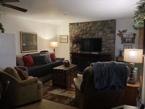 Una sala de estar con chimenea de piedra, televisor y un sofá con cojines.