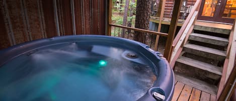 A hot tub on a wooden deck with a view of a forest.