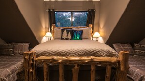 Un dormitorio con una cama grande, dos mesitas de noche con lámparas, una ventana con cortinas y un cabecero de madera.