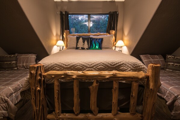 A bedroom with a large bed, two bedside tables with lamps, a window with curtains, and a wooden headboard. - BEAR CREEK LODGE - Make Bear Creek Lodge Your first choice (Broken Bow)