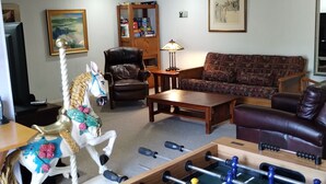 A living room with a foosball table, a sofa, a chair, and a decorative horse. - Spacious and Comfortable Family Home – Close to Beach, Golf, 1.5 blocks to beach (Seaside)