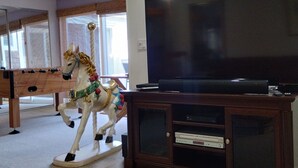 A living room with a large flat-screen TV on a wooden stand, a horse carousel, and a pool table. - Spacious and Comfortable Family Home – Close to Beach, Golf, 1.5 blocks to beach (Seaside)