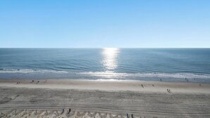 Une plage où des gens se promènent le long du rivage, un ciel dégagé et l’océan en arrière-plan.