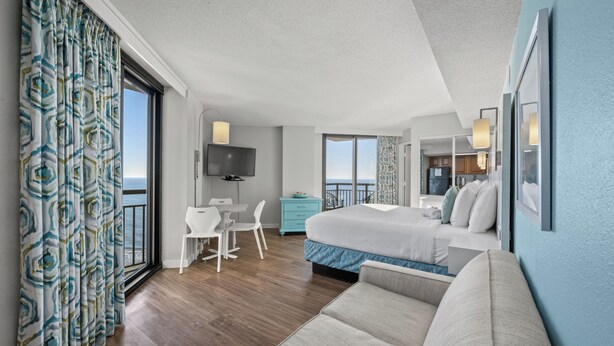 Une chambre d’hôtel avec un lit, un bureau, une chaise, une télévision et un balcon avec vue.