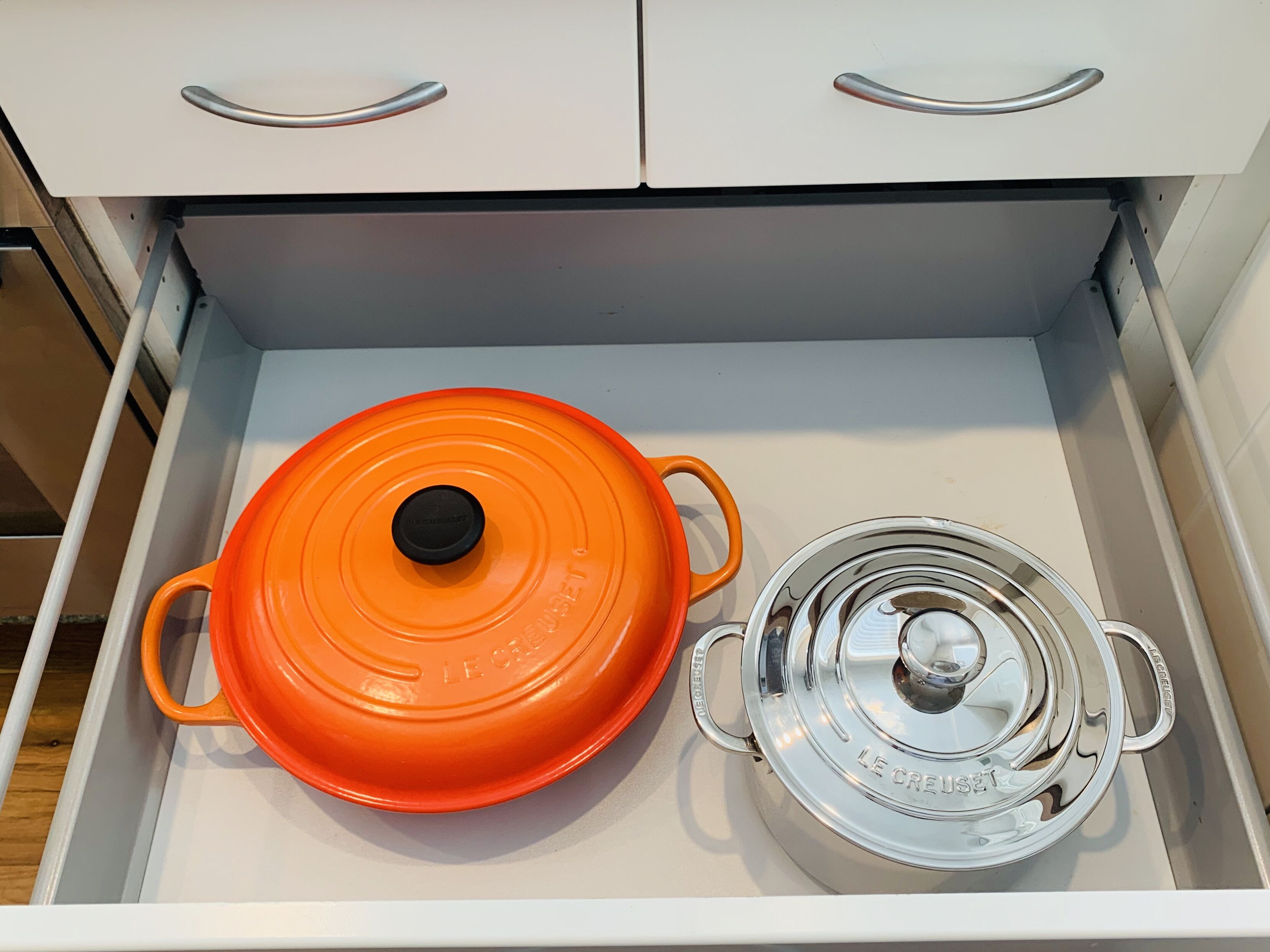Eine Schublade mit einem weißen und einem orangefarbenen Topf, jeweils mit Deckel.