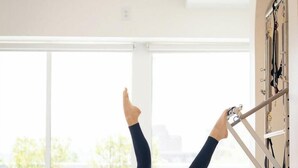 A person performing Pilates on a reformer machine in a room with large windows and a view of greenery. - Palm House- Prime Setting and 5 Stars (Charleston)