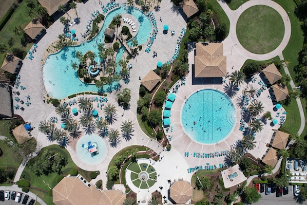 An aerial view of a resort with multiple swimming pools, lounge areas, and palm trees.