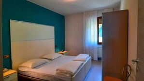 A hotel room with a bed, a nightstand, a window with curtains, and a door. - Appartamento 108 Benaco (Tignale)