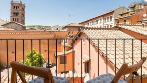 En balkon med to træstole, et tagtækket tag og udsigt til historiske bygninger samt et kirketårn.