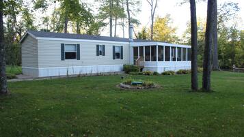 A single-story mobile home with a covered porch, surrounded by a well-maintained lawn and trees.