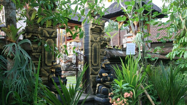 A traditional Balinese temple with stone carvings, a thatched roof, and lush greenery. - Ojeks Homestay (Ubud)