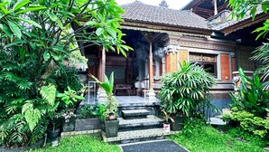 A traditional wooden building with a tiled roof, surrounded by lush greenery and a well-maintained garden. - Ojeks Homestay (Ubud)
