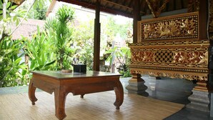 A traditional wooden table in a room with ornate golden carvings and a tiled floor. - Ojeks Homestay (Ubud)