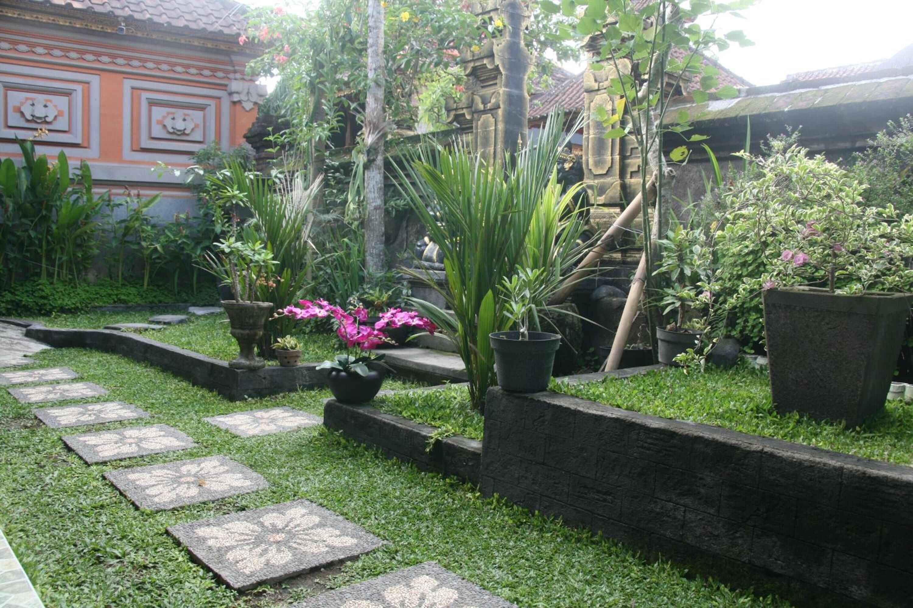 A garden with stone pathways, potted plants, and a traditional building with decorative elements.