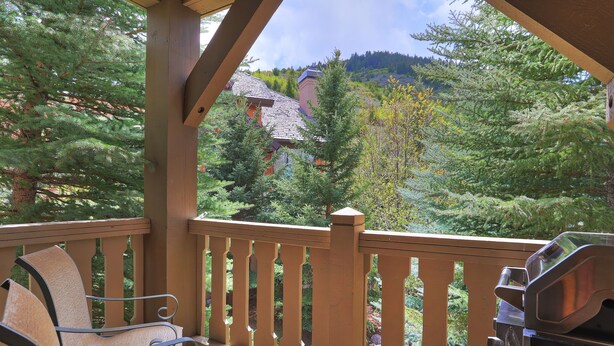 A wooden deck with a chair and grill, overlooking a forested area with a mountain in the background. - 2br- Arrowhead Village- Great Location And Gorgeous  2 Bedroom Condo by RedAwning (Edwards)