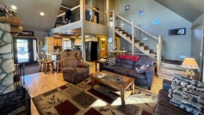 A spacious living area with a high ceiling, a staircase, a dining area, and a kitchen.