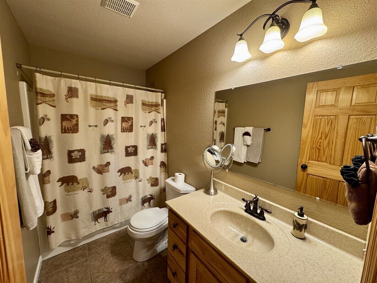 A bathroom with a shower curtain featuring animal prints, a toilet, a sink with a mirror, and a wooden door.