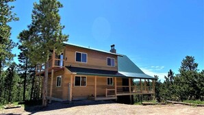 A two-story wooden cabin with a covered porch, surrounded by trees.