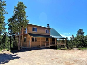 A two-story wooden cabin with a covered porch, surrounded by trees. - Cabin on the Ridge-Game Room, Fireplace, Hot Tub (Lead)