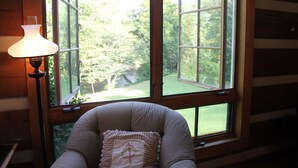 A room with a large window, a chair with a cushion, and a wall-mounted lamp. - Blue Ridge Mountain 'Solitude' on The Little River (Sparta)