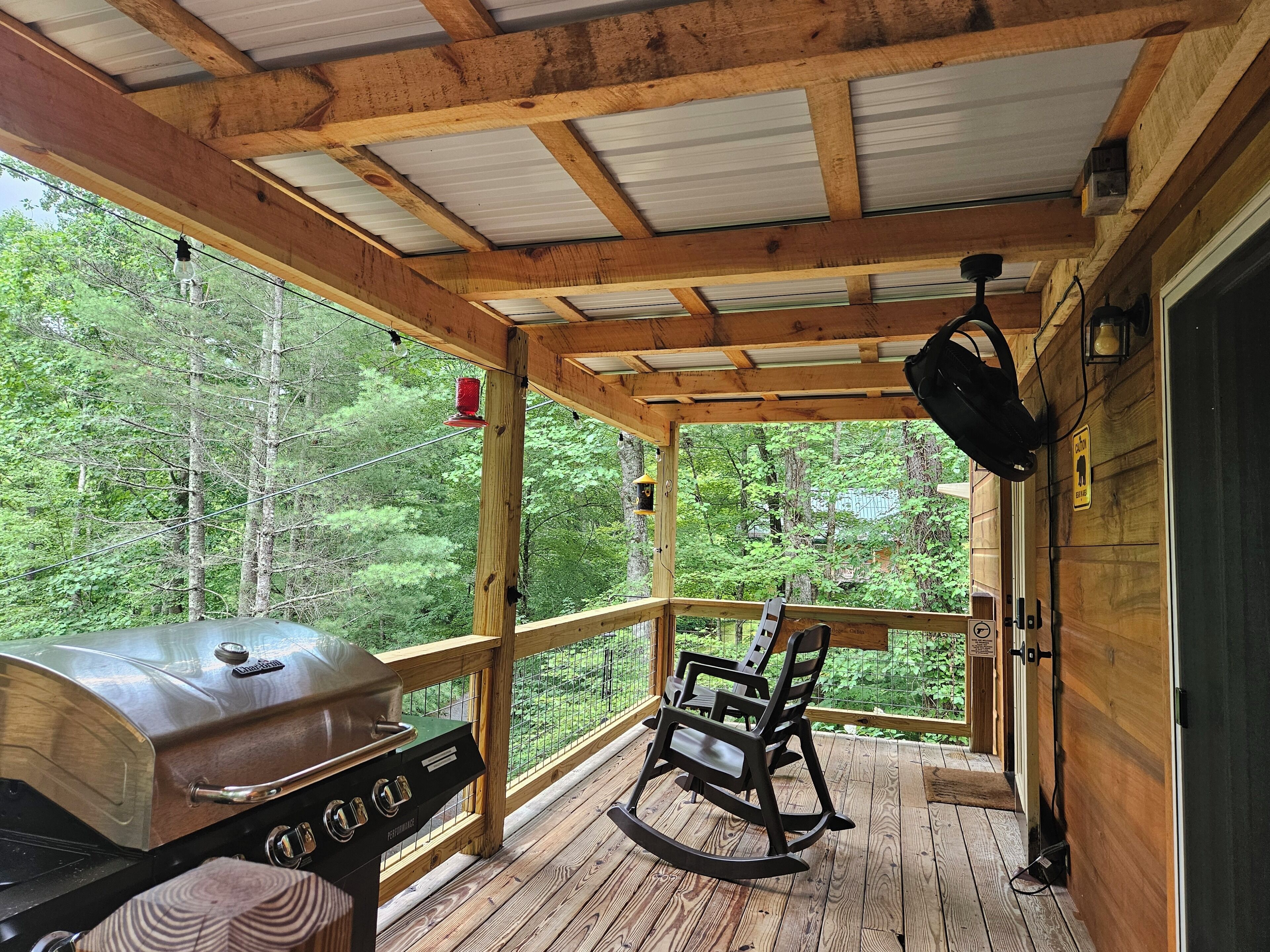 A wooden deck with a grill, rocking chairs, and a view of the forest.