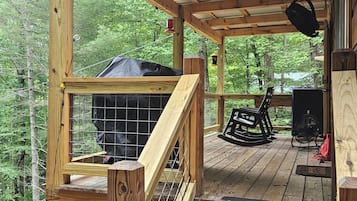 A wooden deck with a grill area, a rocking chair, and a fan.