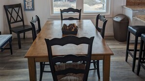 Un coin repas comprenant une table en bois, six chaises, un lustre et une fenêtre avec des stores.