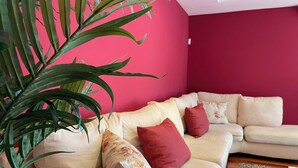 A living room with a beige sofa, red cushions, and a large green plant.