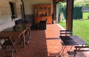 Une terrasse extérieure avec une table et des chaises en verre, un meuble en bois et un sol carrelé.