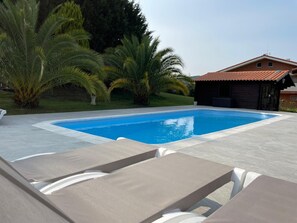 A swimming pool with lounge chairs, surrounded by palm trees and a building with a tiled roof.