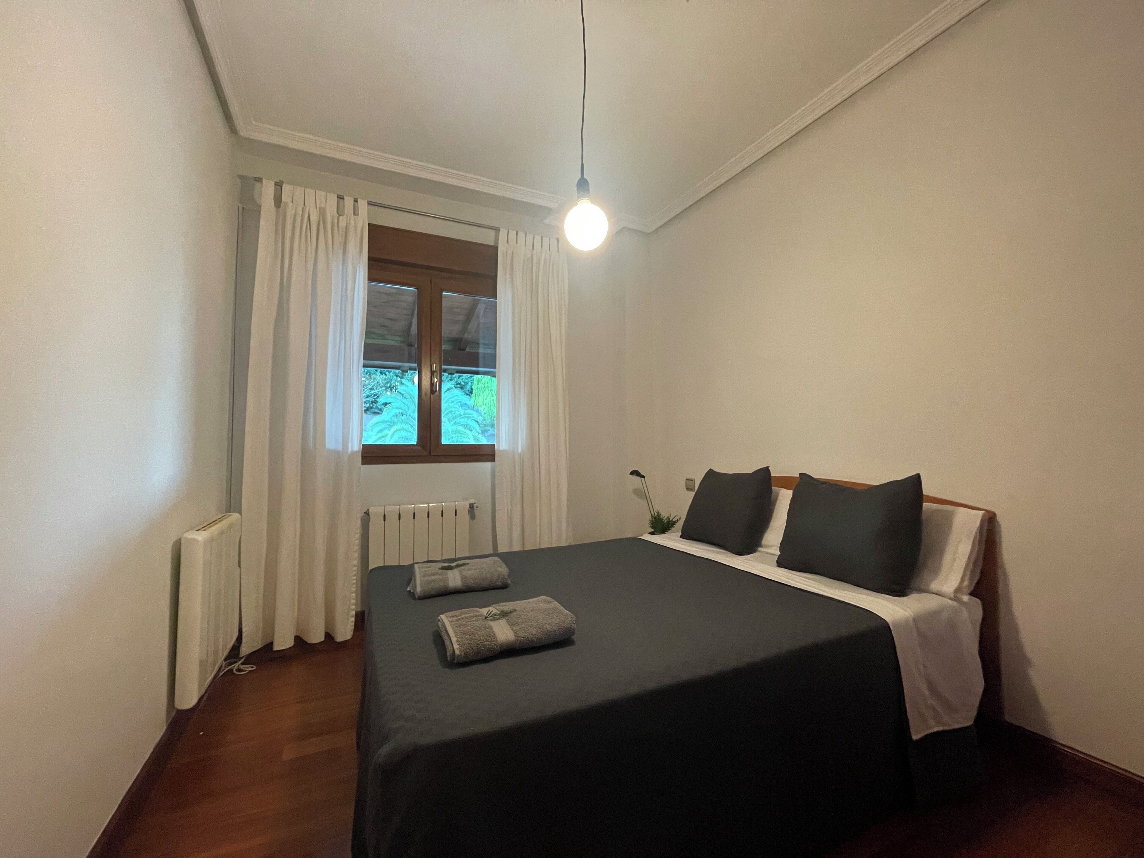 Een hotelkamer met een bed, een radiator, een raam met gordijnen en een bedlamp.
