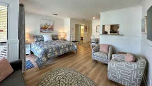 Une chambre à coucher comprenant un lit, des tables de chevet, une chaise, un canapé, un tapis à motifs et un tableau accroché au mur.