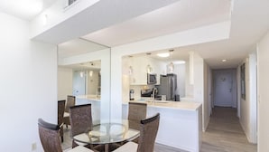 A modern kitchen with a central island, dining area with wicker chairs, and a hallway leading to another room.