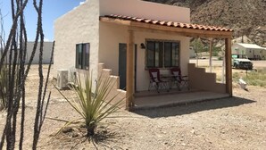 A small, single-story building with a tiled roof and a patio area with two chairs and a table. - Big Bend Bungalow A (TERLINGUA)