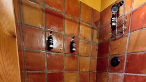 A shower area with tiled walls and floor, a wooden door, and a metal shelf with toiletries. - Big Bend Bungalow A (TERLINGUA)