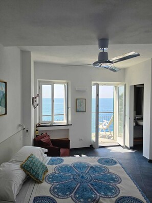 Ein Schlafzimmer mit Bett, Deckenventilator, Fenster mit Meerblick und offener Tür zum Balkon.