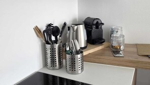 Een keuken met een zwart inductiefornuis, roestvrijstalen keukengerei in houders, een koffiezetapparaat en een pot met kruiden op een houten plank.