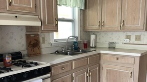 A kitchen with wooden cabinets, a stove, a sink, and a window with a green valance. - Single family home - Less than 4 miles from Rehoboth Beach Boardwalk (Rehoboth Beach)