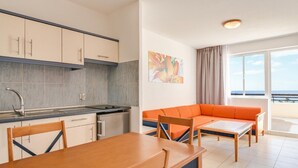 A modern kitchen with a dining area, a sofa, and a large window with a view. - Apartments Palm Garden (Morro Jable)