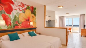 A hotel room with a large bed, a dining area, and a view of the ocean. - Apartments Palm Garden (Morro Jable)
