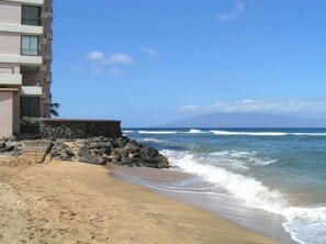 A beach with a building on the left, waves crashing onto the shore, and a clear sky.