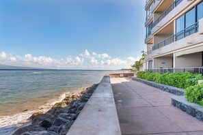 Um hotel na praia com um calçadão de concreto que leva ao oceano, uma varanda com vista para o mar e um edifício com vários andares.