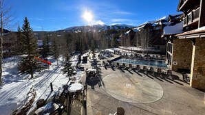 A resort with outdoor seating and a pool, surrounded by snow-covered mountains and trees.