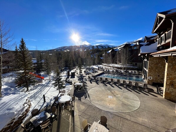 A resort with outdoor seating and a pool, surrounded by snow-covered mountains and trees.