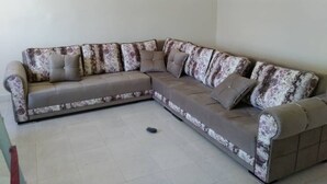 A L-shaped sectional sofa with a floral pattern, positioned in a room with a tiled floor and a framed picture on the wall. - Beach site apartment (Nouackchott)