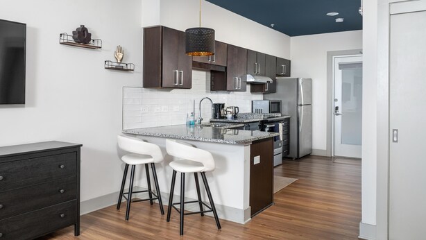 Une cuisine moderne avec des meubles de couleur sombre, un plan de travail en granit et un luminaire suspendu.