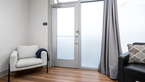 Un salon moderne avec un canapé, un fauteuil, une porte-fenêtre coulissante et une fenêtre avec des rideaux.