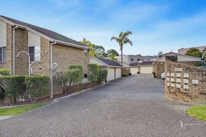 A residential street with houses, a gravel driveway, and a brick wall with a sign.